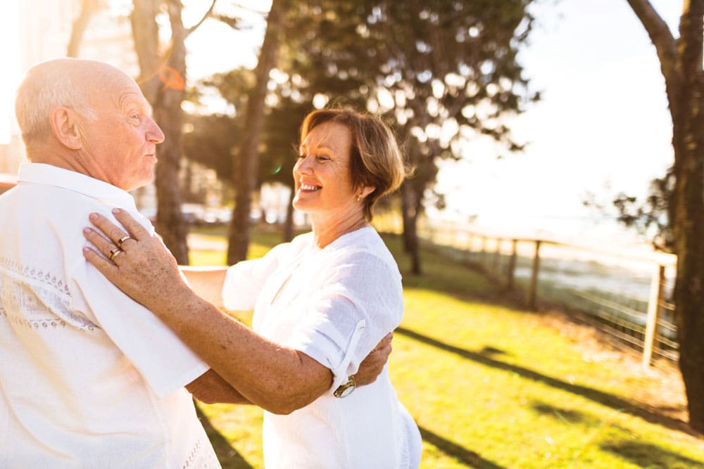 Charter Senior Living of Franklin Residents couple dressed all in white smiles and dances together outdoors 